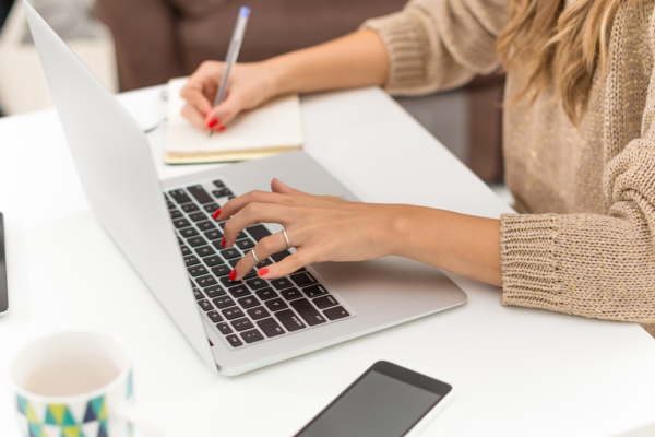 Photo of a marketing director taking notes in a notebook while reviewing information on her laptop